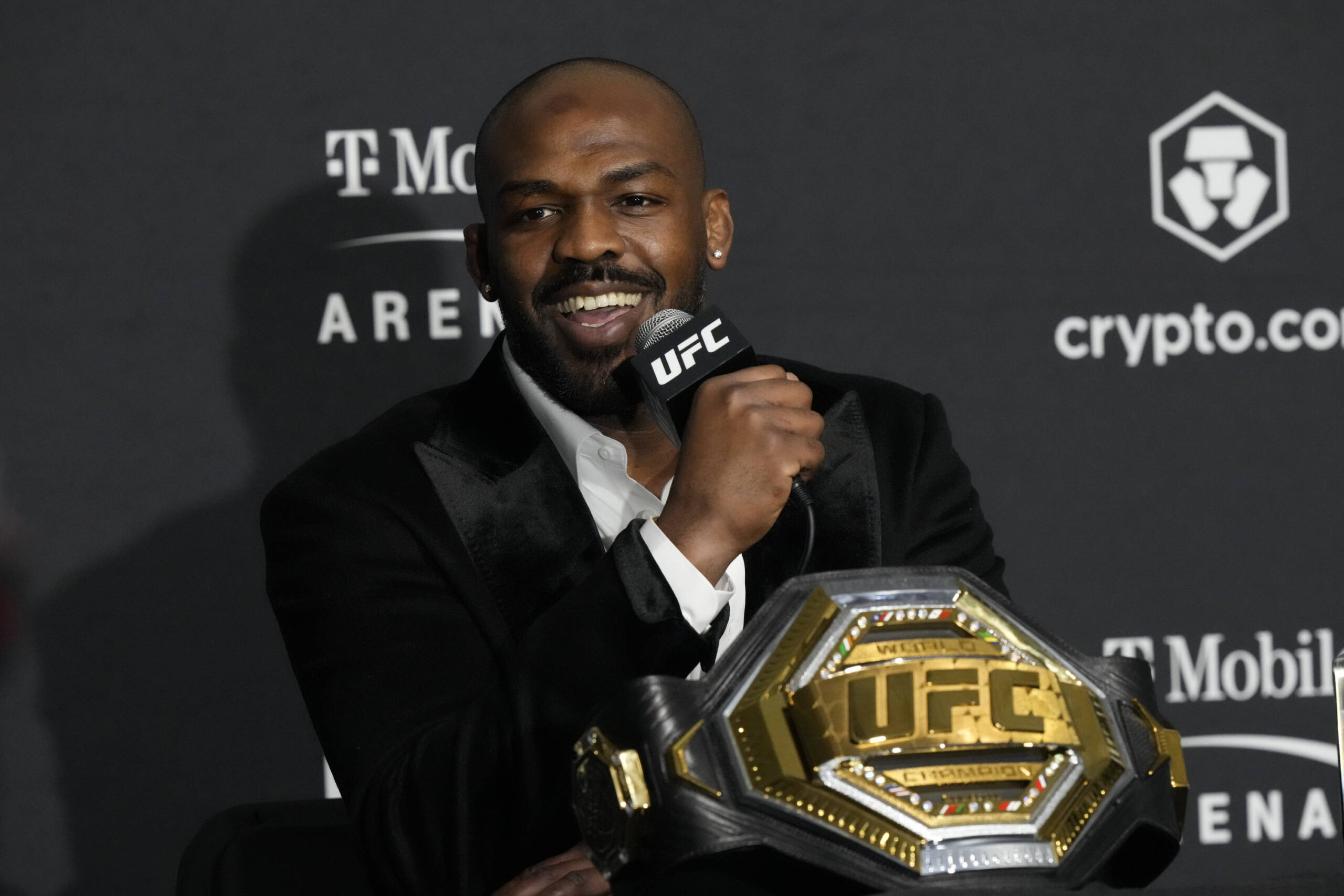 Jon Jones speaking into a UFC microphone with his UFC belt on the table