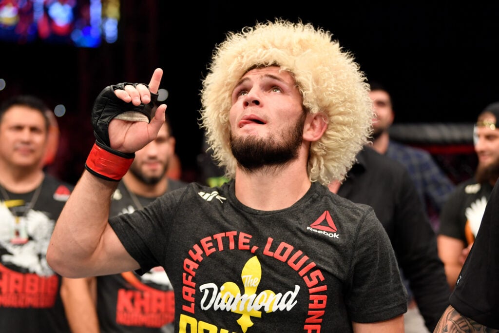 Khabib Nurmagomedov points to the sky while wearing a yellow wig and a 'Lafayette, Louisiana' Dustin 'Diamond' Poirier t-shirt