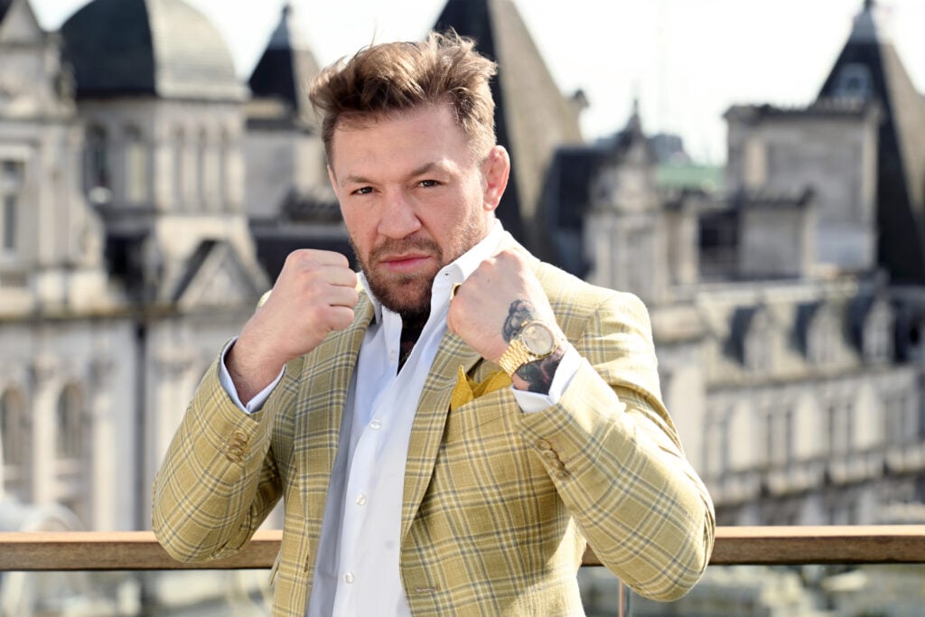 Conor McGregor wearing a yellow suit poses with his fists raised in a fighting stance