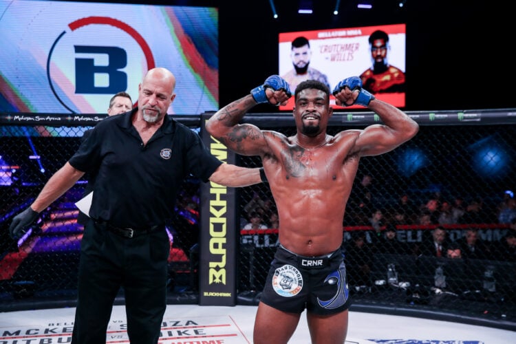 Jaleel Willis, shirtless, flexes his muscles to celebrate winning an MMA fight, with a referee standing next to him