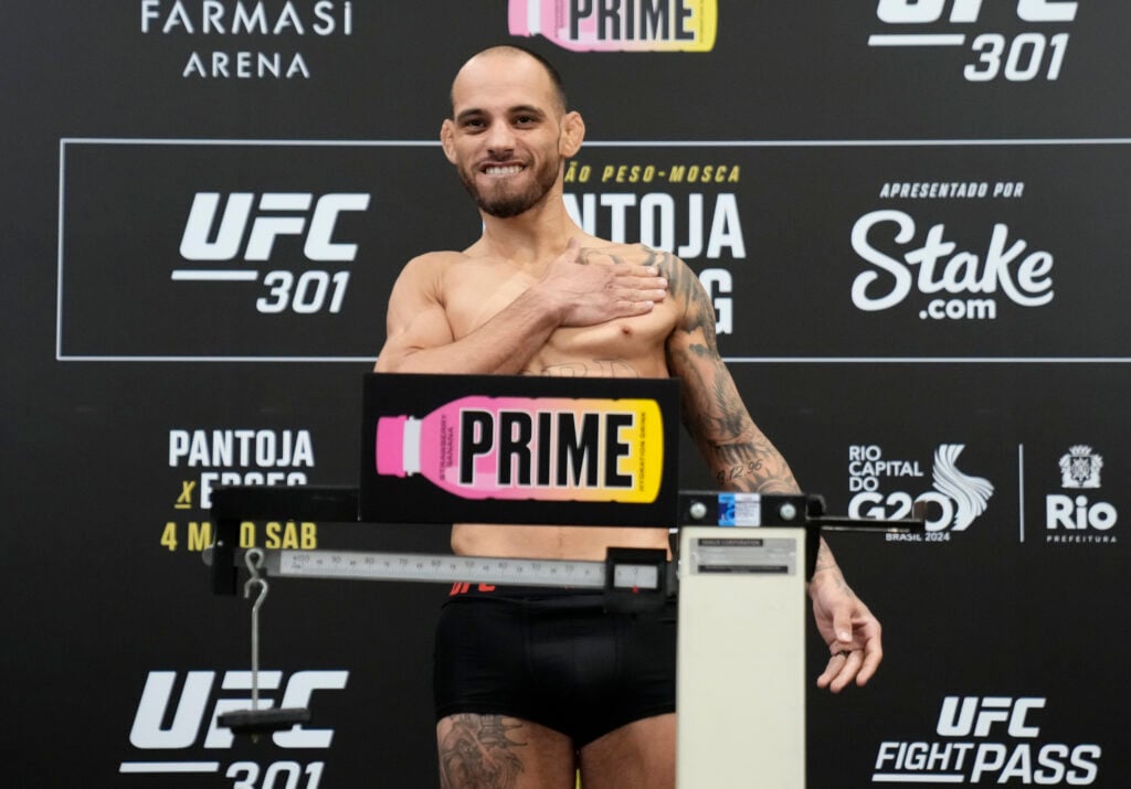 Jean Silva beats his chest while standing on a scale with 'Prime' branding in front of UFC advertising boards