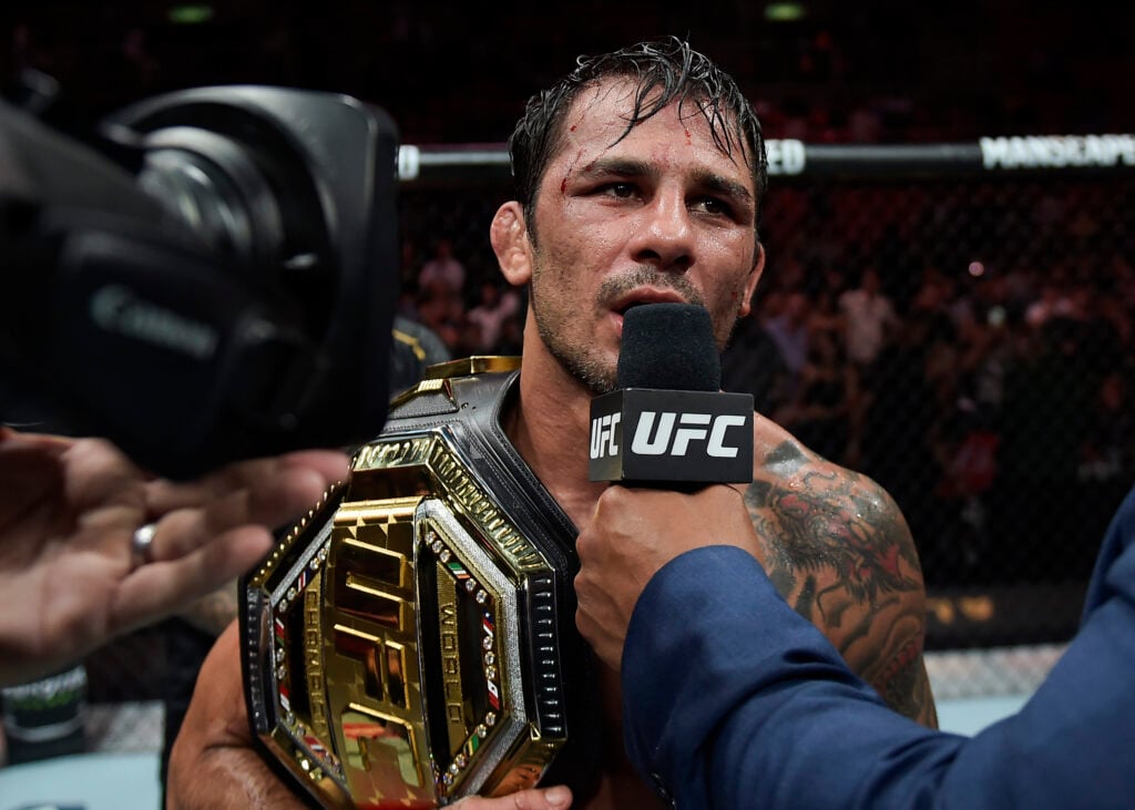 Alexandre Pantoja with his UFC title belt on his arm speaks into a UFC-branded microphone