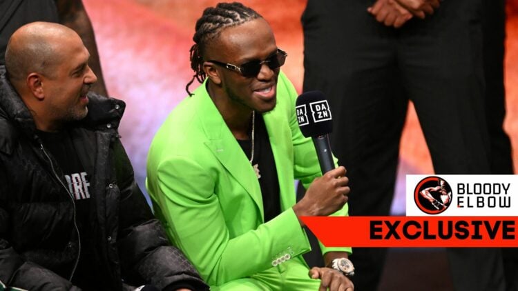 KSI in a green suit laughs while holding a DAZN microphone, with Mams Taylor in a puffa jacket to his right