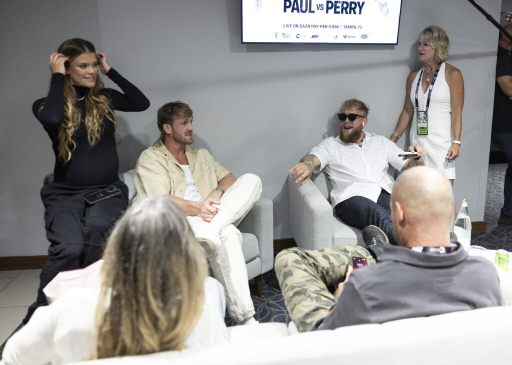 Logan Paul and Jake Paul sitting backstage talking with Nina Agdal (left) and Pam Stepnick (right) standing with them