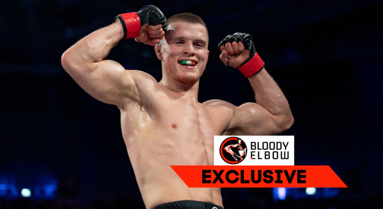 Paul Hughes flexing after winning his Bellator debut. Overlay text reads "Bloody Elbow EXCLUSIVE"