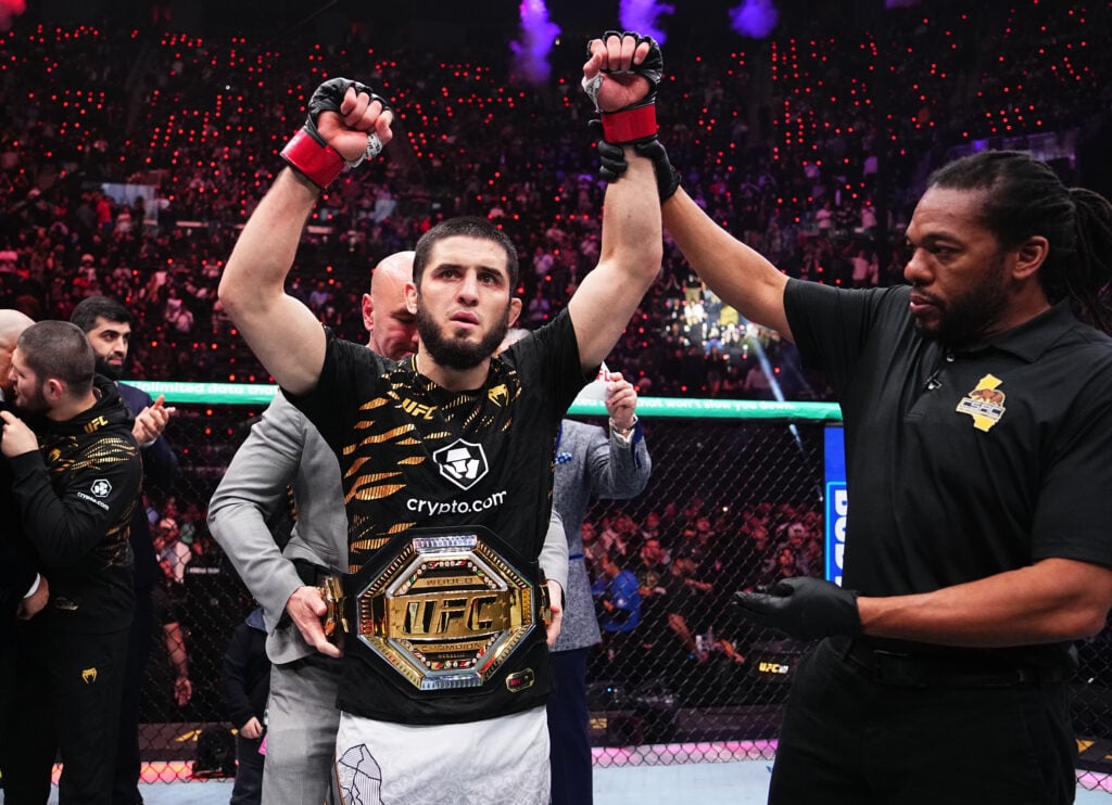 Islam Makhachev wearing the UFC title belt has his hand held aloft as winner at UFC 311 by referee Herb Dean
