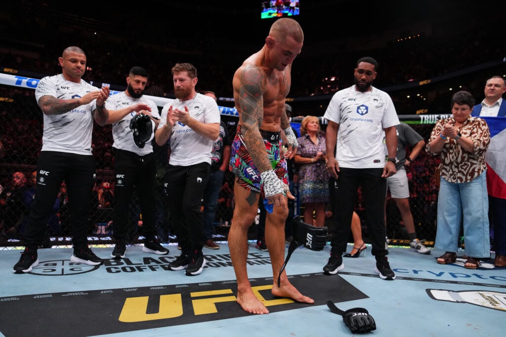 Dustin Poirier lays his gloves down in the UFC octagon after his final fight, with teammates applauding in the background