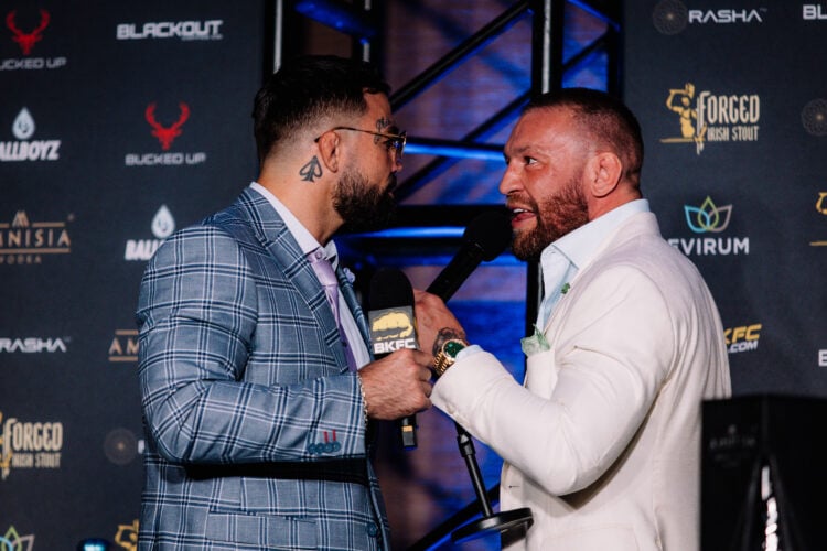 Mike Perry, wearing a grey suit and sunglasses, facing off with Conor McGregor in a white suit