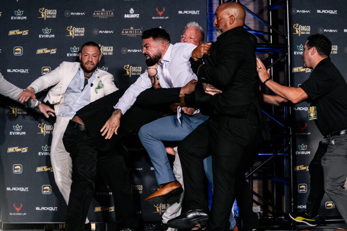 Conor McGreogr watches on as security hold back an angry Mike Perry.