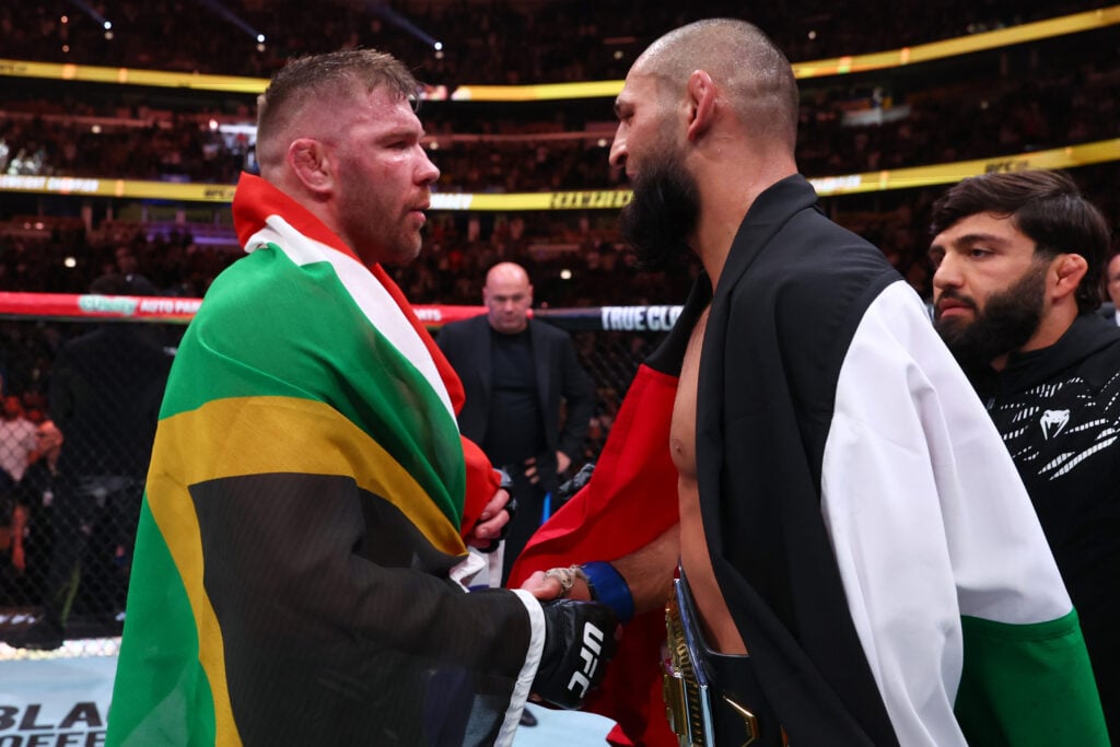 Dricus Du Plessis draped in a South African flag shakes hand with Khamzat Chimaev in a UAE flag after their fight at UFC 319
