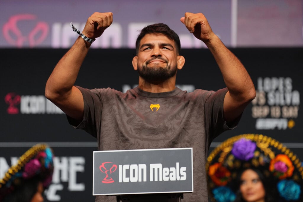 Kelvin Gastelum smirks and raises his hands on the scales at Noche UFC ceremonial weigh-ins