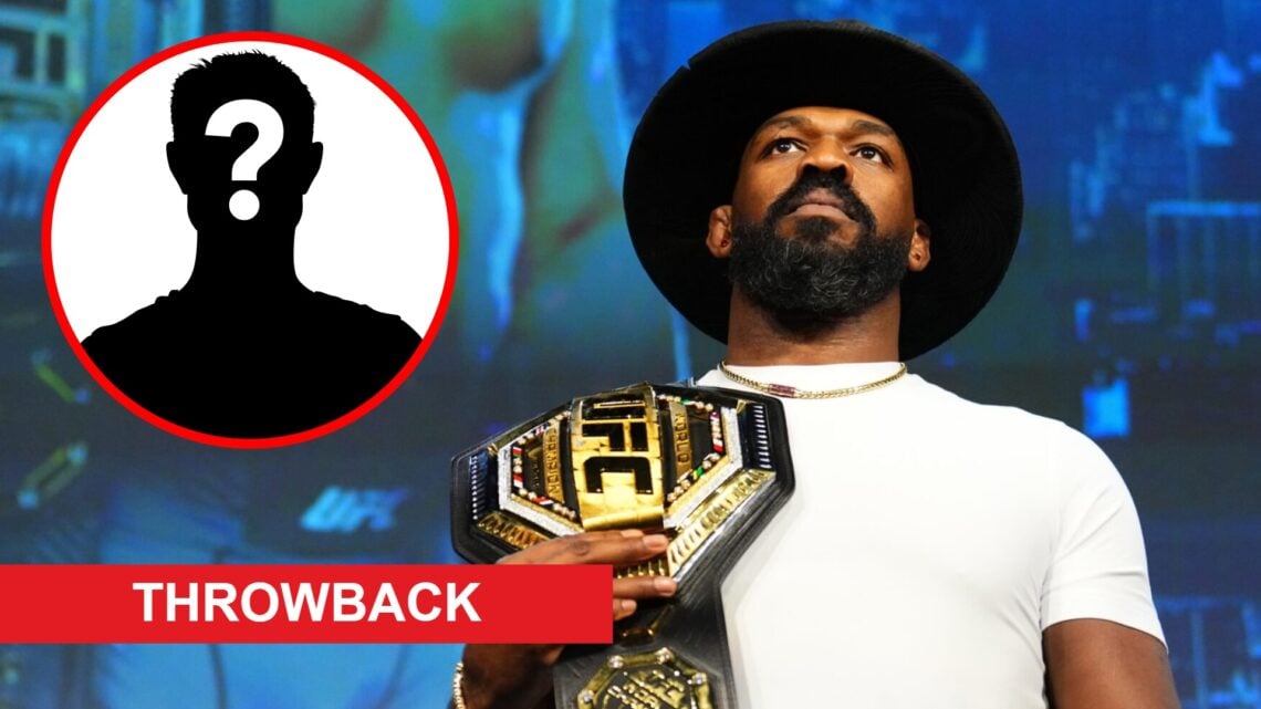 Jon Jones poses onstage at the UFC 309 press conference, inset mystery icon and throwback banner