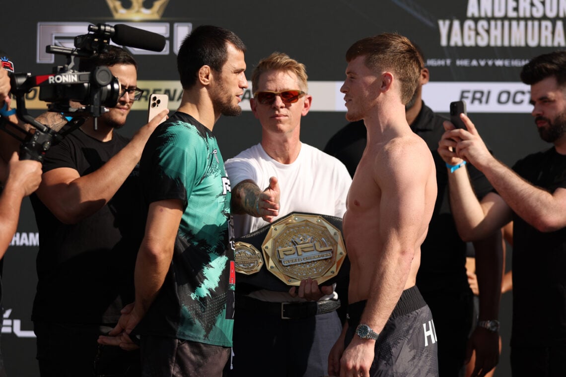 Usman Nurmagomedov, wearing a t-shirt, faces off with Paul Hughes, shirtless, as John Martin stands between them holding the PFL belt