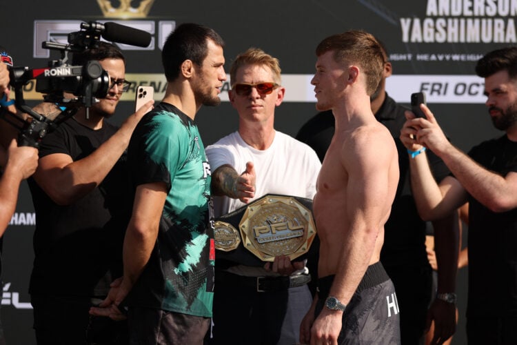 Usman Nurmagomedov, wearing a t-shirt, faces off with Paul Hughes, shirtless, as John Martin stands between them holding the PFL belt