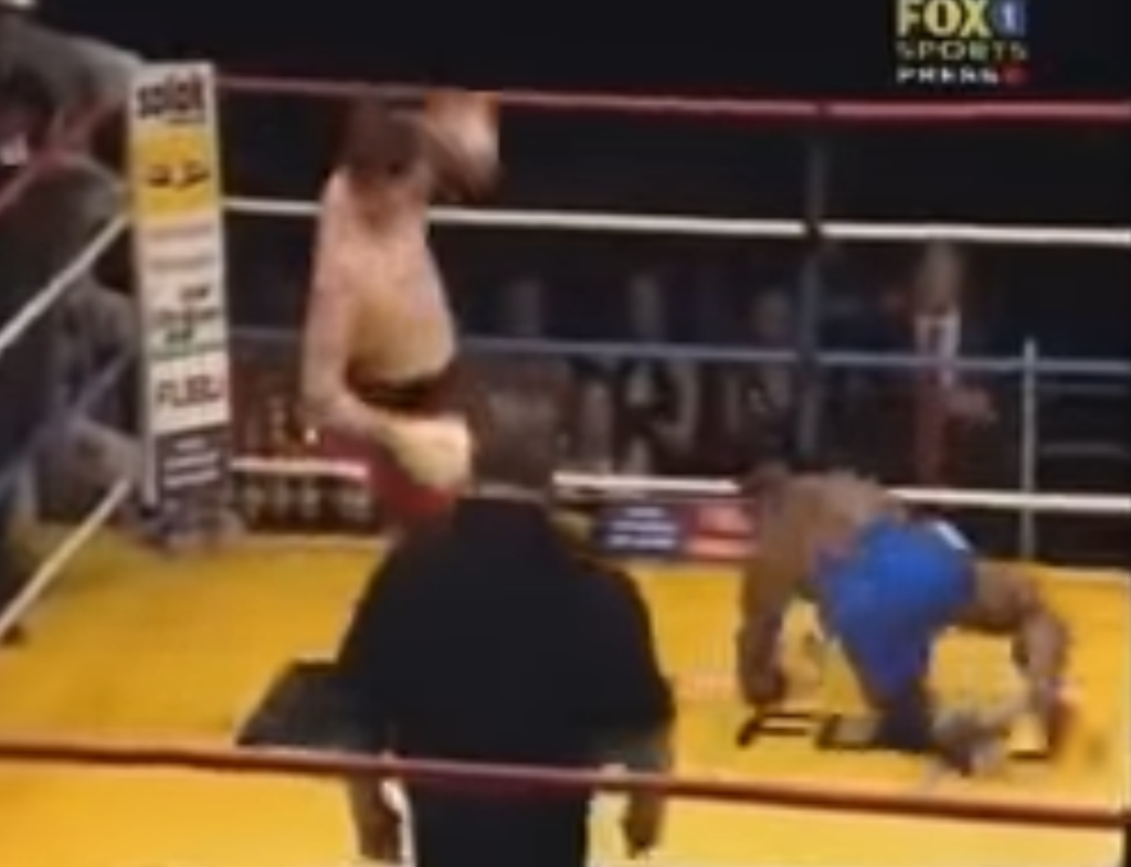 Kickboxer Stanley Nandex lands a kick against his opponent, who bounces off the ropes and is still flailing. 