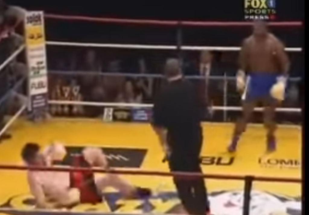 Kickboxer Stanley Nandex stands and watches his opponent, who is dazed on the canvas.